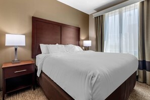 Une chambre d’hôtel avec un grand lit, deux tables de chevet avec des lampes, une tête de lit en bois et une fenêtre avec des rideaux.