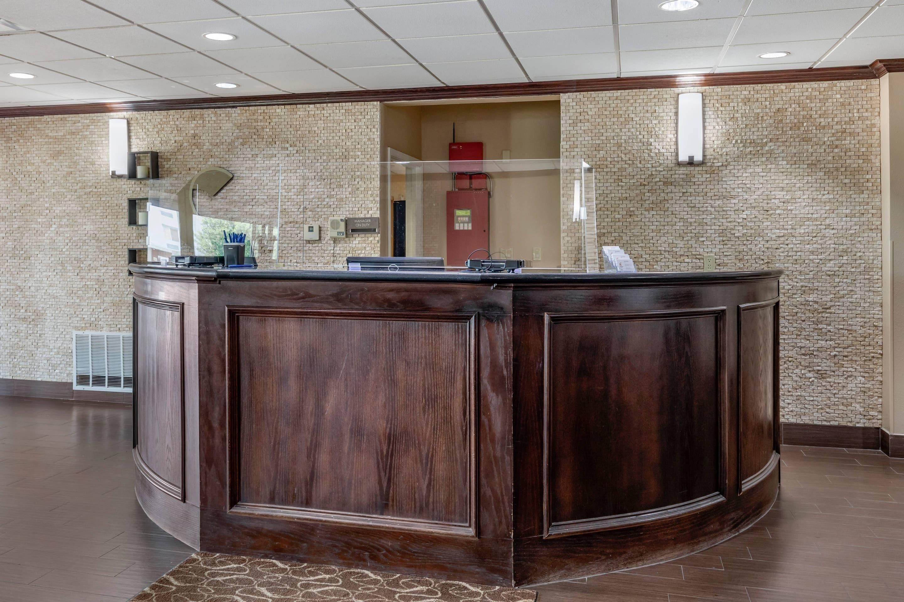 A reception desk with a dark wood finish, a glass partition, and a brick wall background.