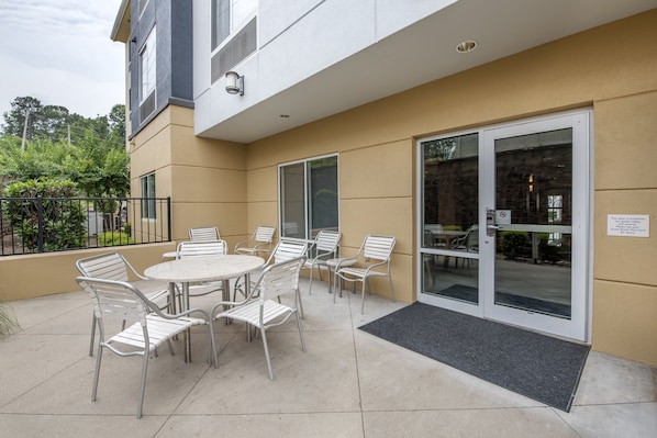An outdoor patio with a round table and chairs, a glass door entrance, and a black mat at the door. - Comfort Suites Plano - Dallas North (Plano)