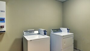 A laundry room with two white washing machines and a utility cart. - Comfort Suites Plano - Dallas North (Plano)