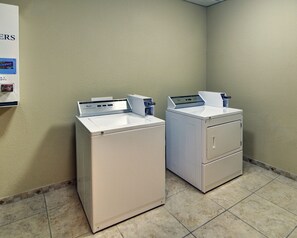 A laundry room with two white washing machines and a utility cart. - Comfort Suites Plano - Dallas North (Plano)
