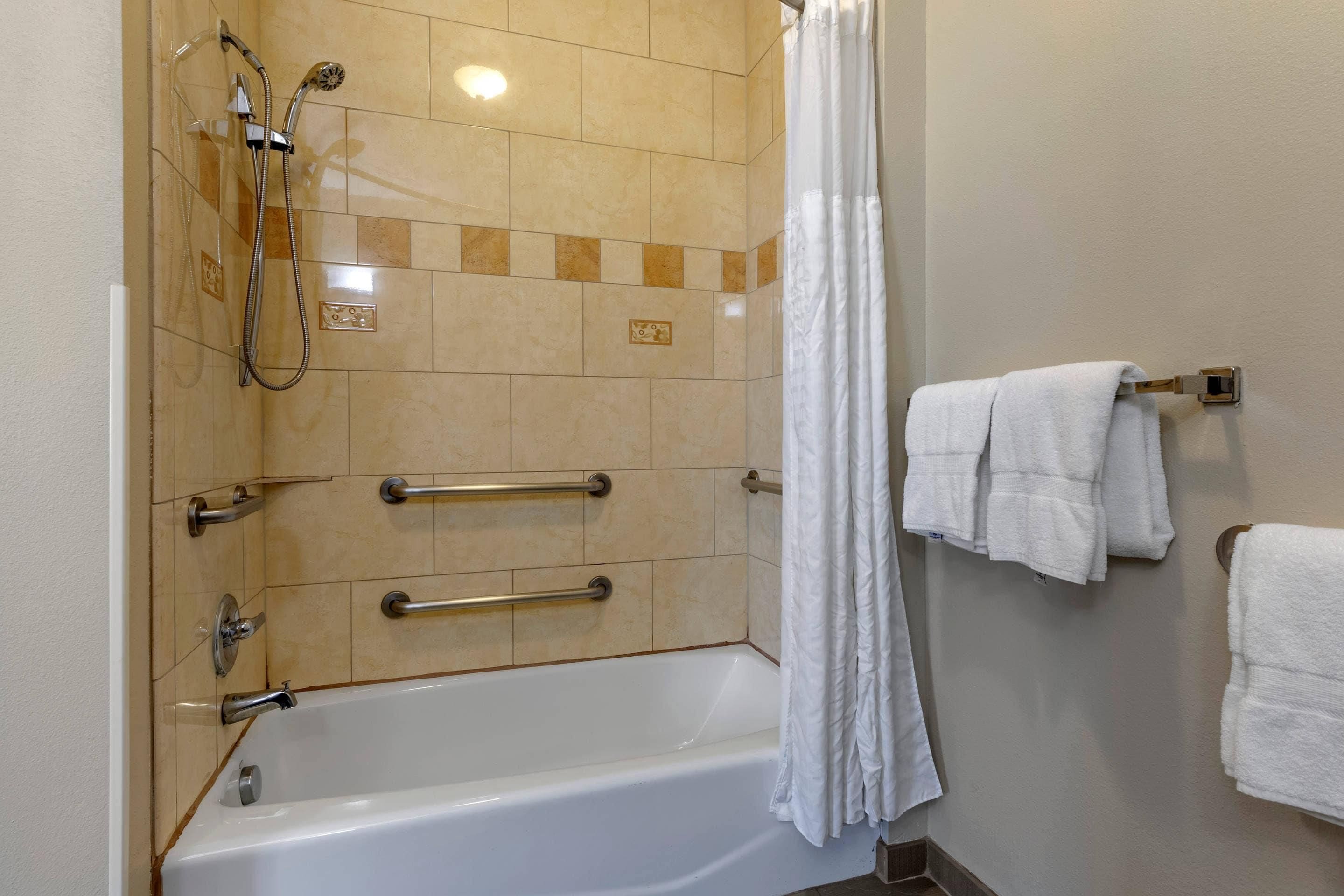 A bathroom with a bathtub, a shower with a handheld showerhead, grab bars, and a towel rack with towels.