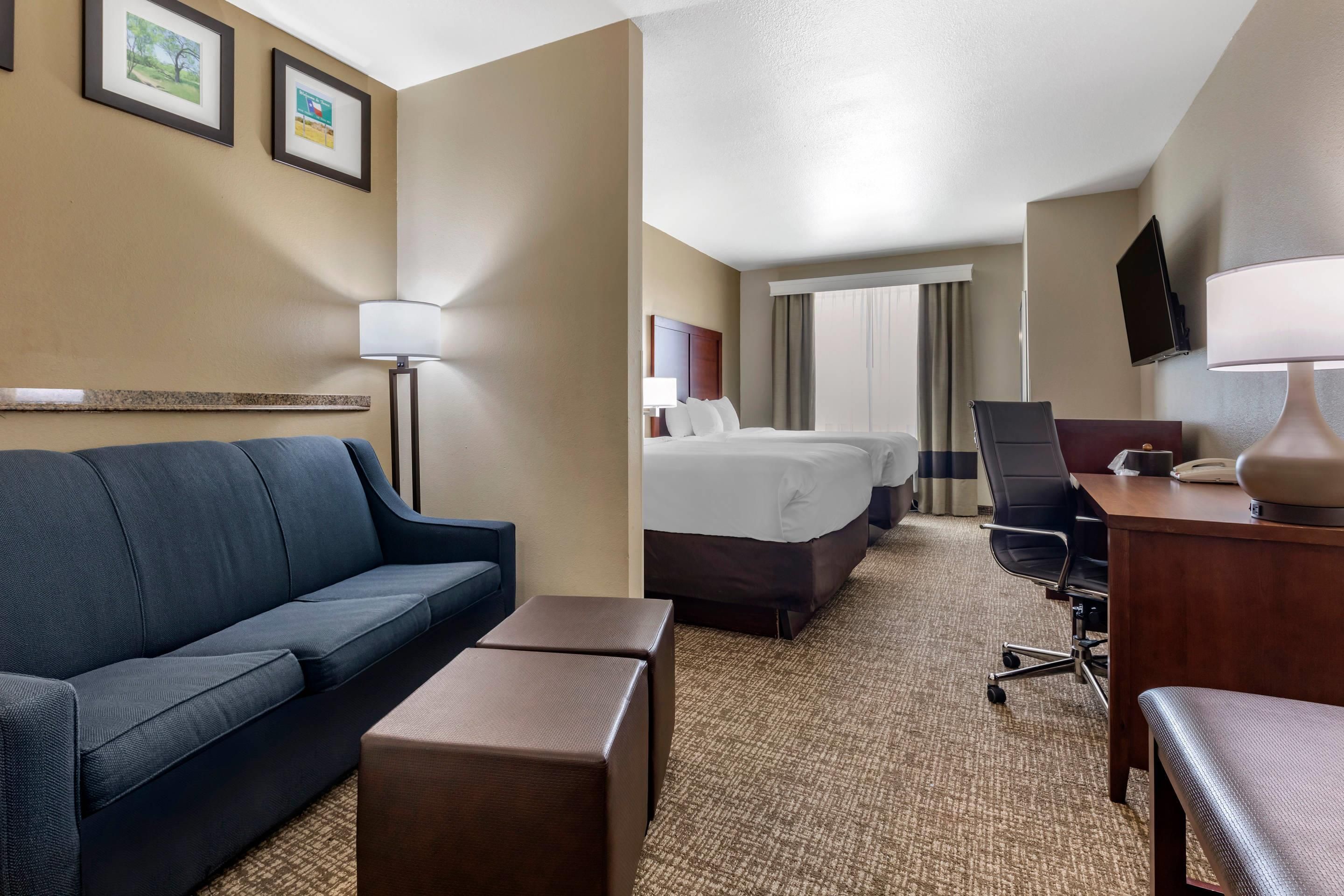 A hotel room with a blue sofa, a small table, a bed with two pillows, a desk with a chair, and a TV mounted on the wall.
