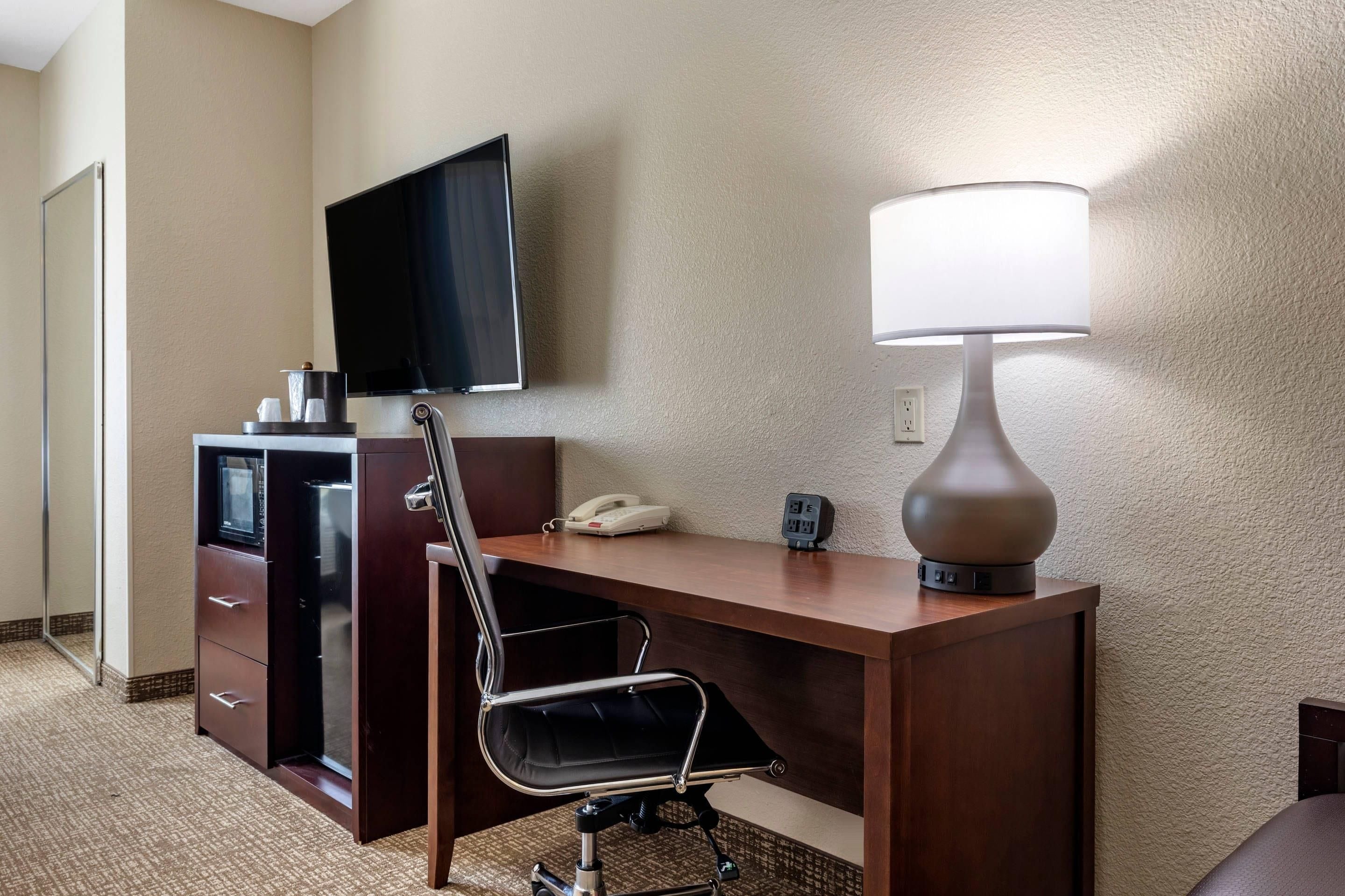 A hotel room with a desk, chair, television, lamp, and a telephone.