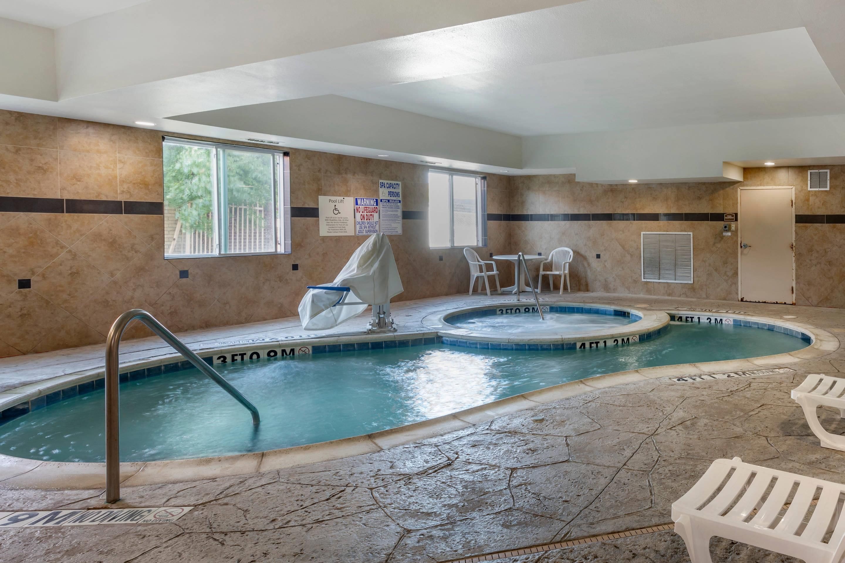 Una piscina interior con elevador de piscina, dos sillas y una zona cubierta.