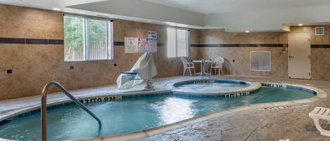 An indoor swimming pool with a pool lift, two chairs, and a covered area.