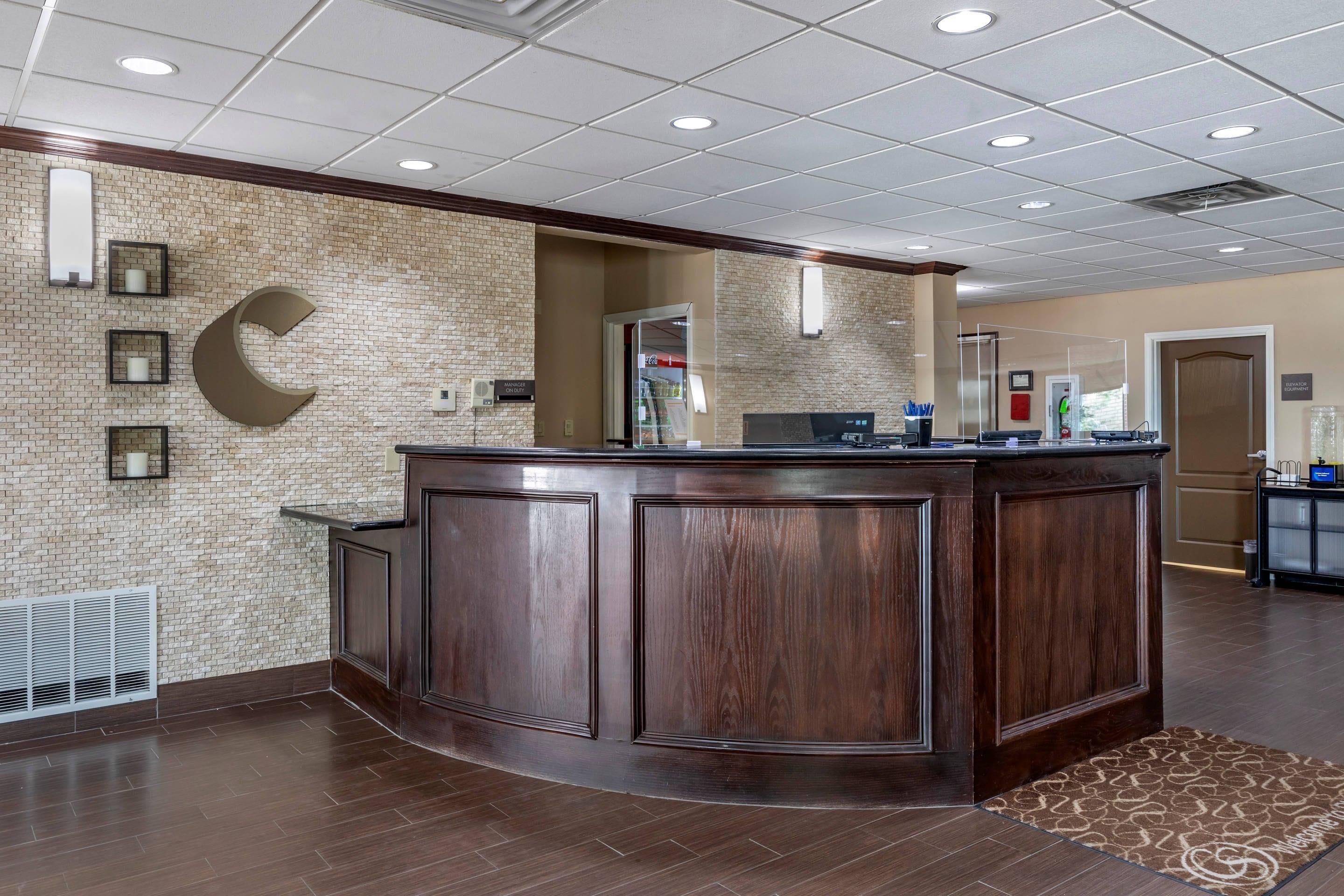 A reception area with a dark wood reception desk, a brick wall, and a ceiling with recessed lighting.