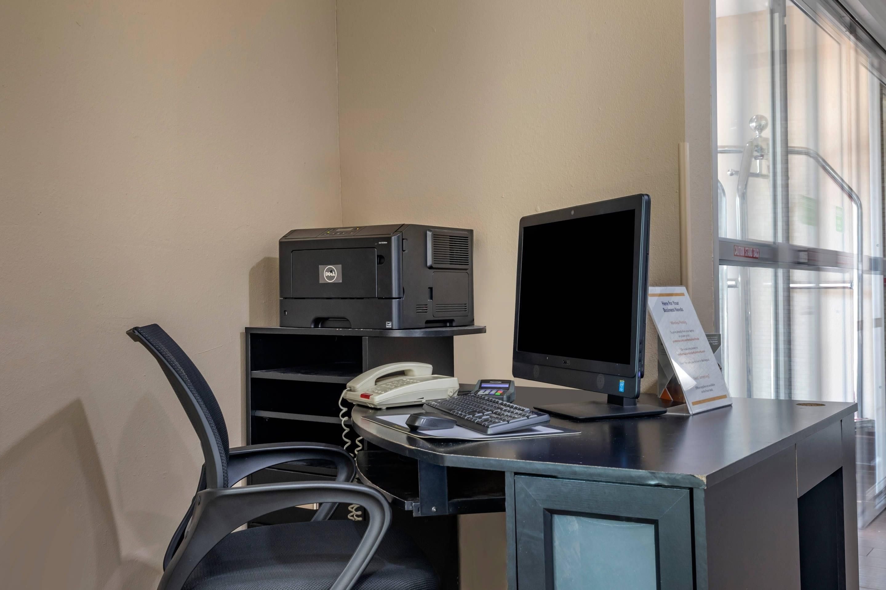 Un bureau dans une chambre d’hôtel, avec un ordinateur, un téléphone et un panneau.