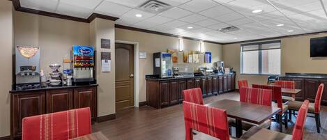 A hotel dining area with multiple tables and chairs, a coffee machine, and a refrigerator.