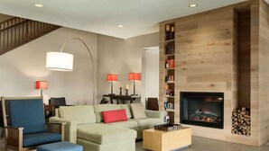 A modern living room with a fireplace, a staircase, and a bookshelf. - Country Inn & Suites by Radisson, Kansas City at Village West, KS (Kansas City)