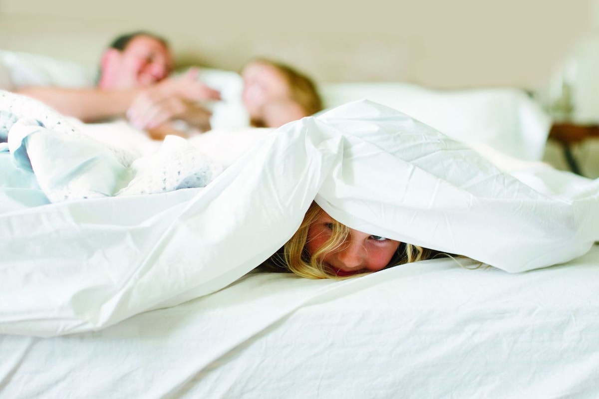 Una cama con ropa de cama blanca y una persona cubierta parcialmente por una manta blanca.