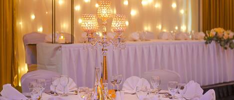 Une table de banquet dressée avec des nappes blanches, des chandeliers dorés et de la verrerie élégante.