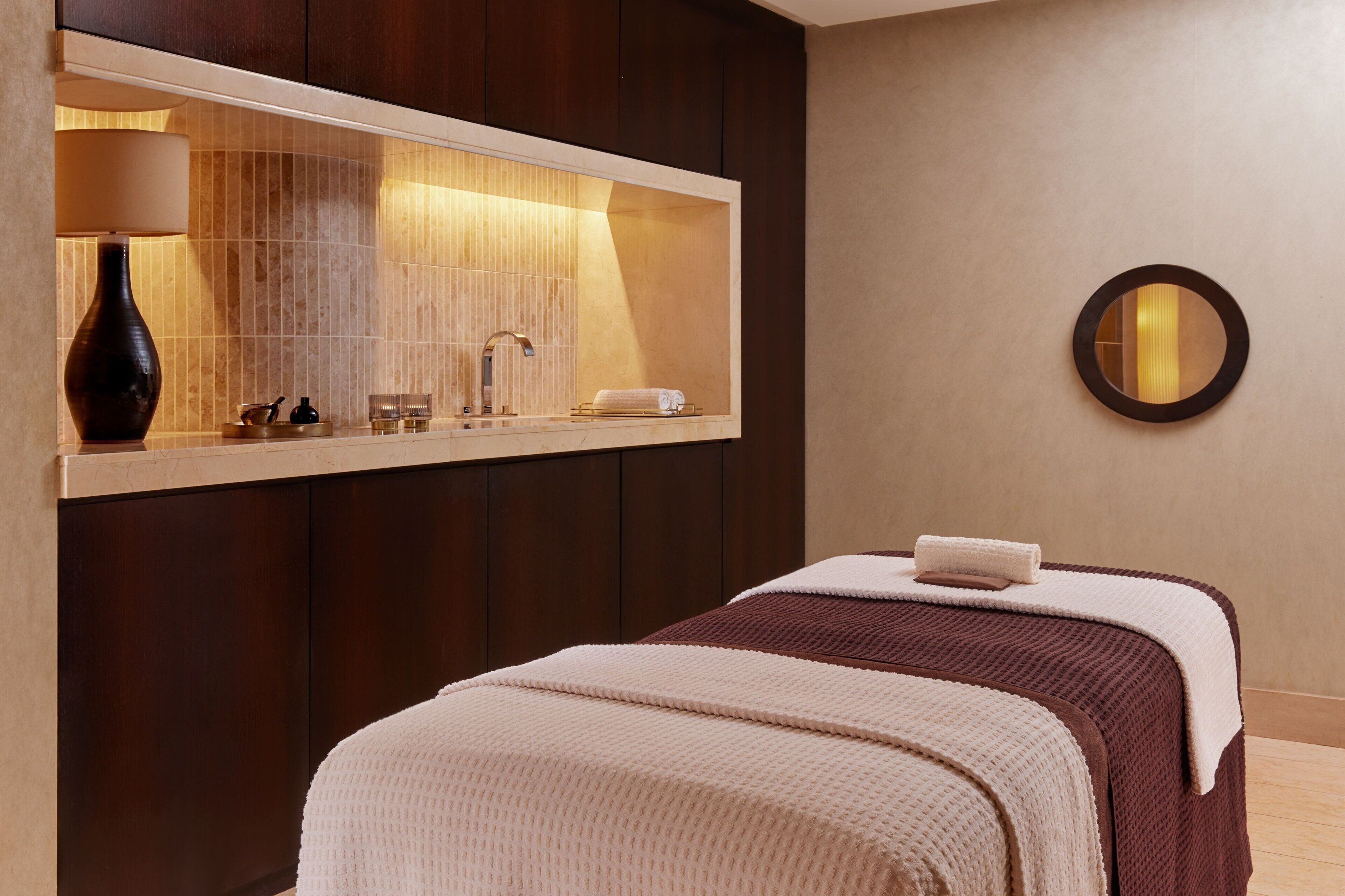 Una habitación de hotel moderna con un espejo grande, una mesita de noche con lámpara y una cama bien hecha.
