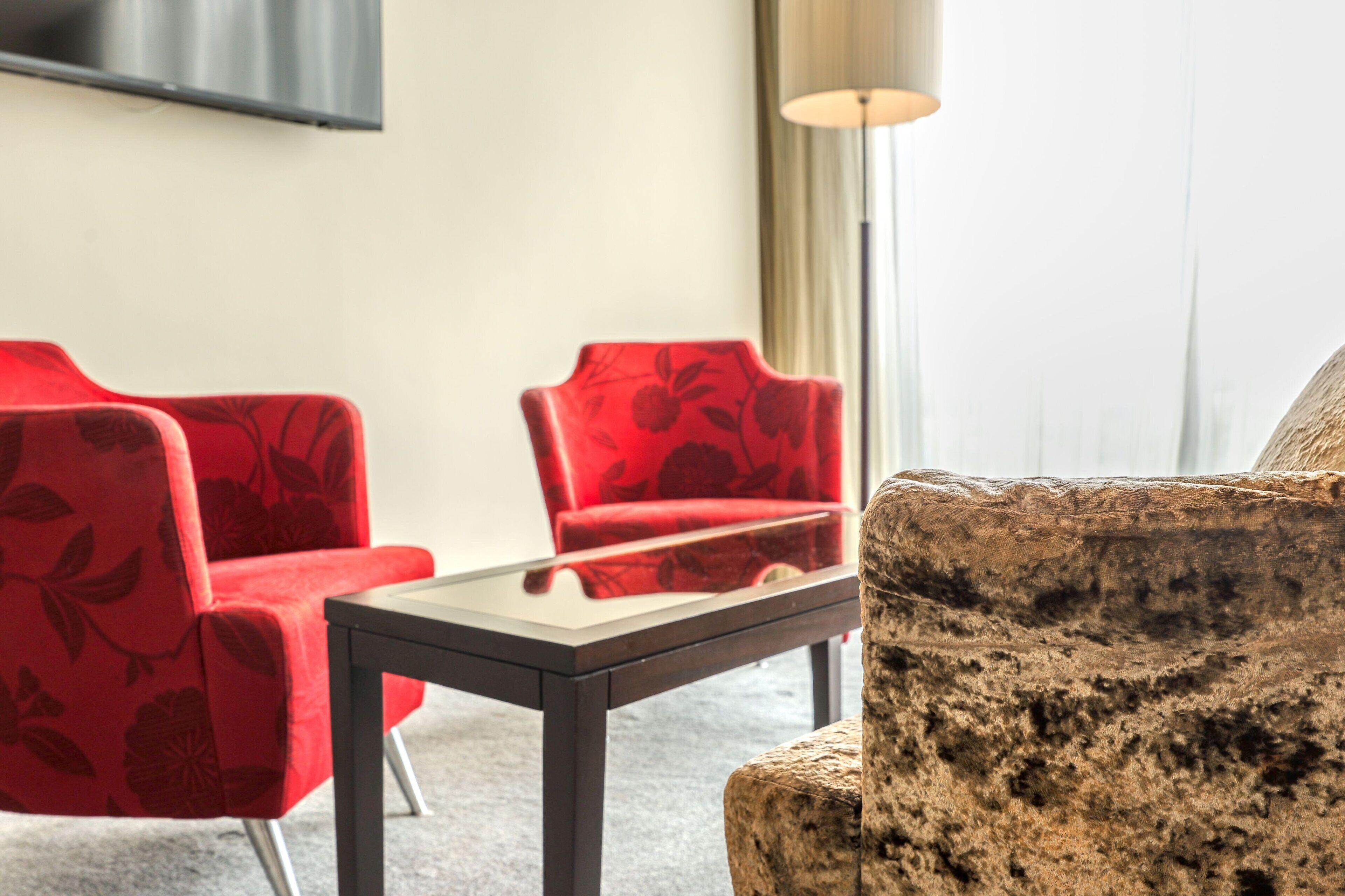 A modern room with a stone accent piece, a glass-top table, and two red upholstered chairs.