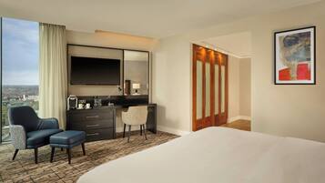A hotel room with a large bed, a desk with a chair, a TV, and a city view.