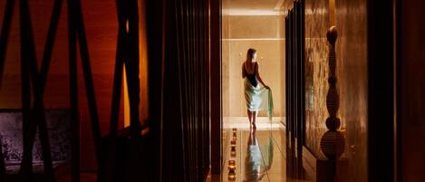 A corridor with a reflective floor, a person walking, and a staircase with decorative elements.