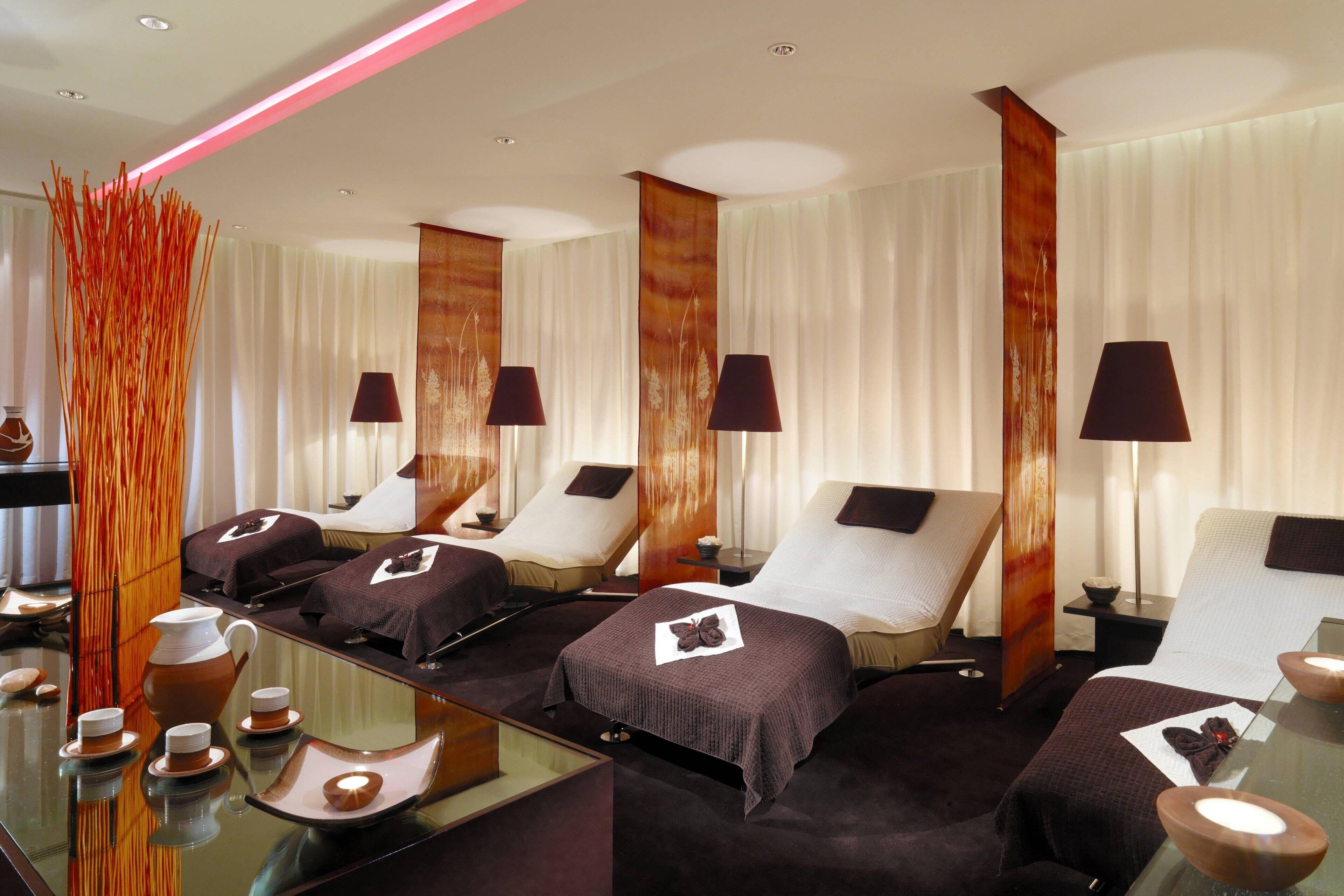 Une salle de spa équipée de plusieurs tables de massage, d’une table en verre avec un service à thé et d’un vase décoratif.