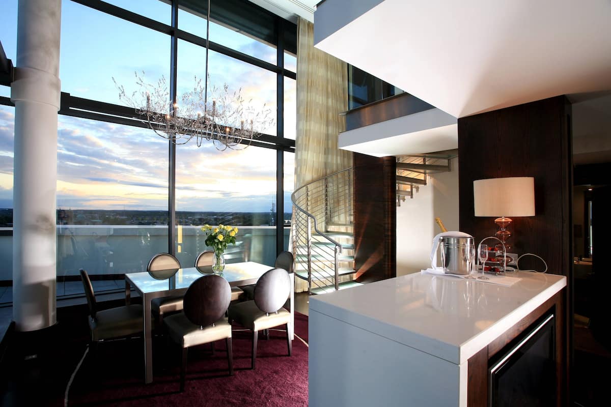 A modern dining area with a table, chairs, and a chandelier. There is a staircase leading to an upper level.