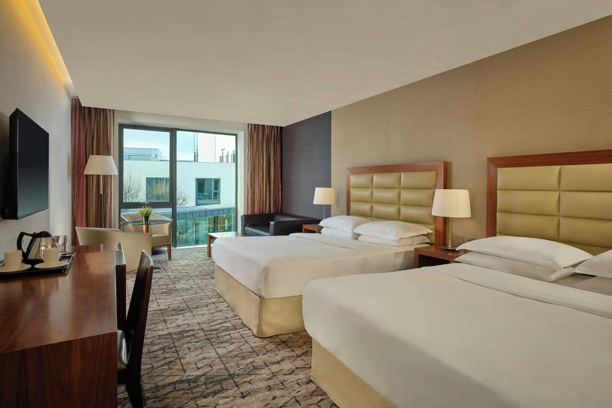 A hotel room with two beds, a desk, a chair, a TV, and a balcony with a view.