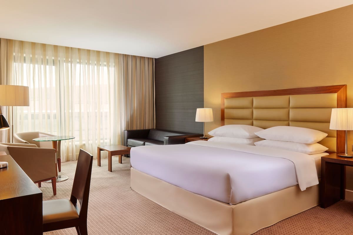 A hotel room with a large bed, a desk with a chair, a small table, a sofa, and a TV.