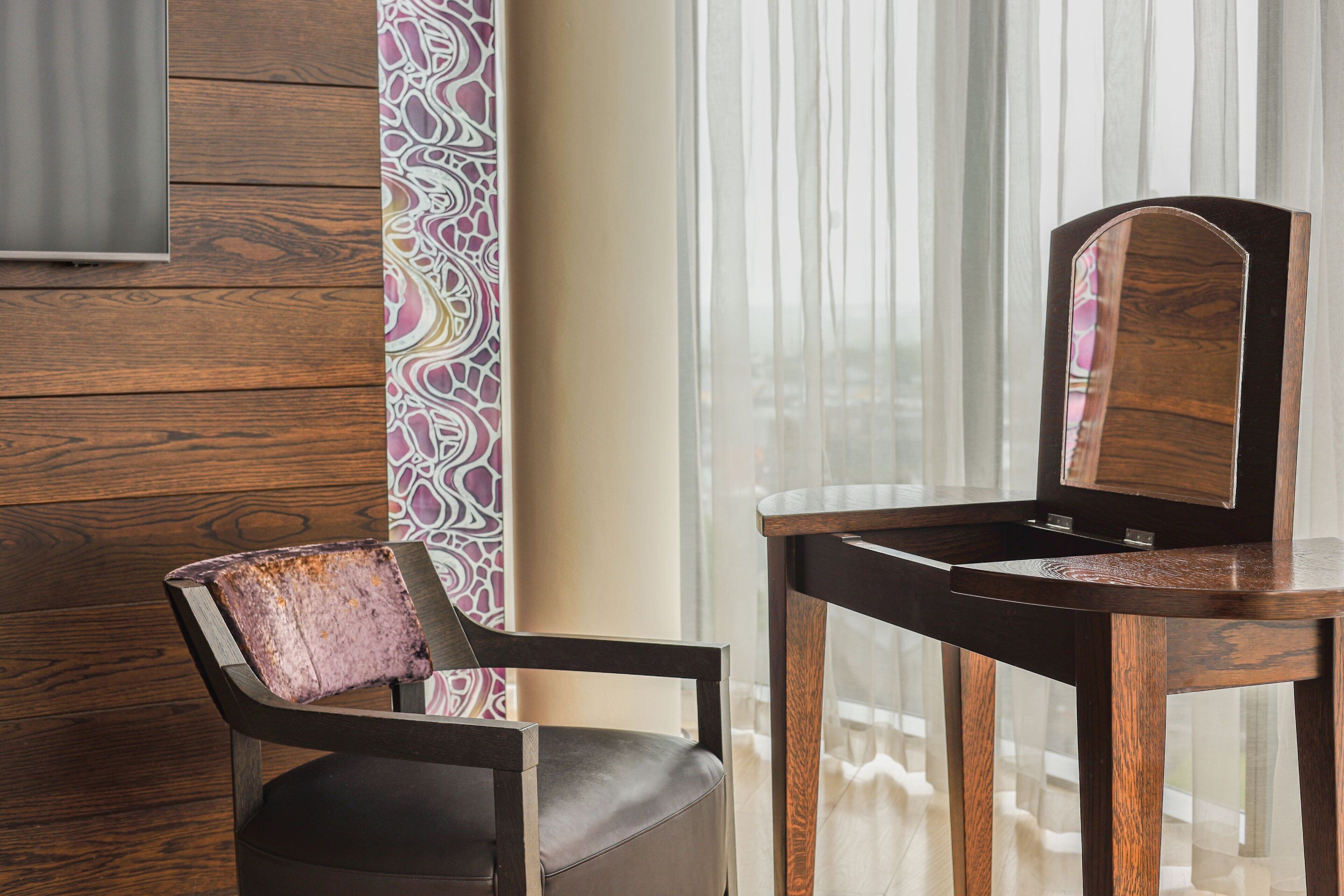 A wooden chair with a cushioned seat and backrest, positioned next to a wooden table with a mirror.