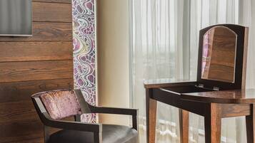A wooden chair with a cushioned seat and backrest, positioned next to a wooden table with a mirror.