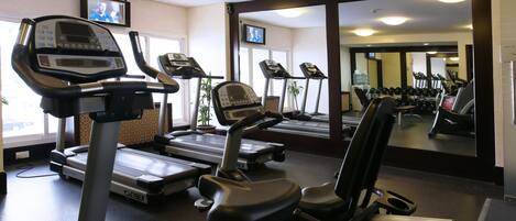 Un gimnasio con cintas de correr, una bicicleta estática y una banca de pesas.