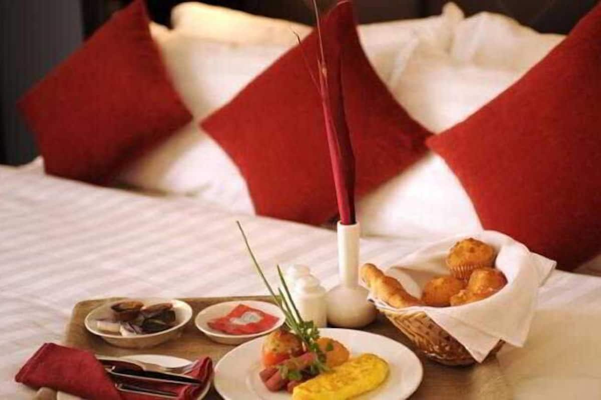 A neatly arranged breakfast table with a variety of food items, including eggs, pastries, and a bottle of milk, set on a bed with red pillows.