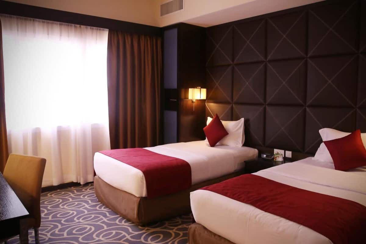 Ein Hotelzimmer mit zwei Betten, einem Schreibtisch und einem großen Fenster mit Vorhängen.