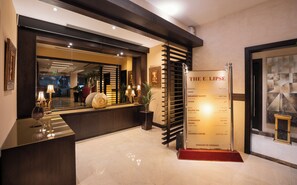 A reception area with a polished reception desk, a mirror, and a wall-mounted information board listing amenities such as a breakfast buffet and spa. - The Eclipse Boutique Suites (Abu Dhabi)