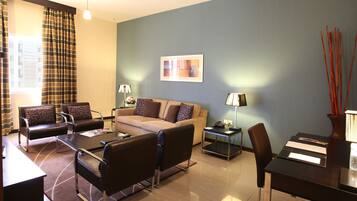 A modern living room with a sofa, two armchairs, a coffee table, and a dining table. There are lamps on side tables and a framed picture on the wall.