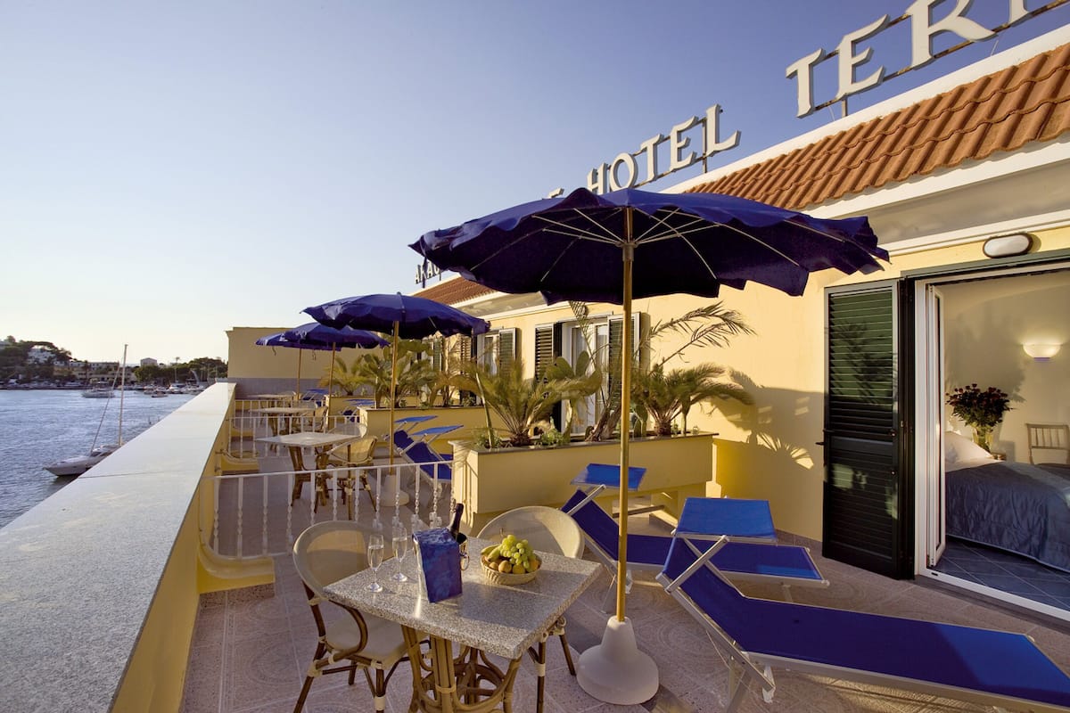 Eine Hotelterrasse mit Außenbestuhlung, einem Pool und Blick aufs Meer.