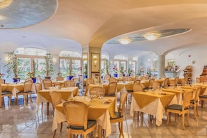 A restaurant with round tables, chairs, and potted plants.