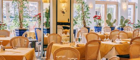 A restaurant with round tables, wicker chairs, and potted plants.