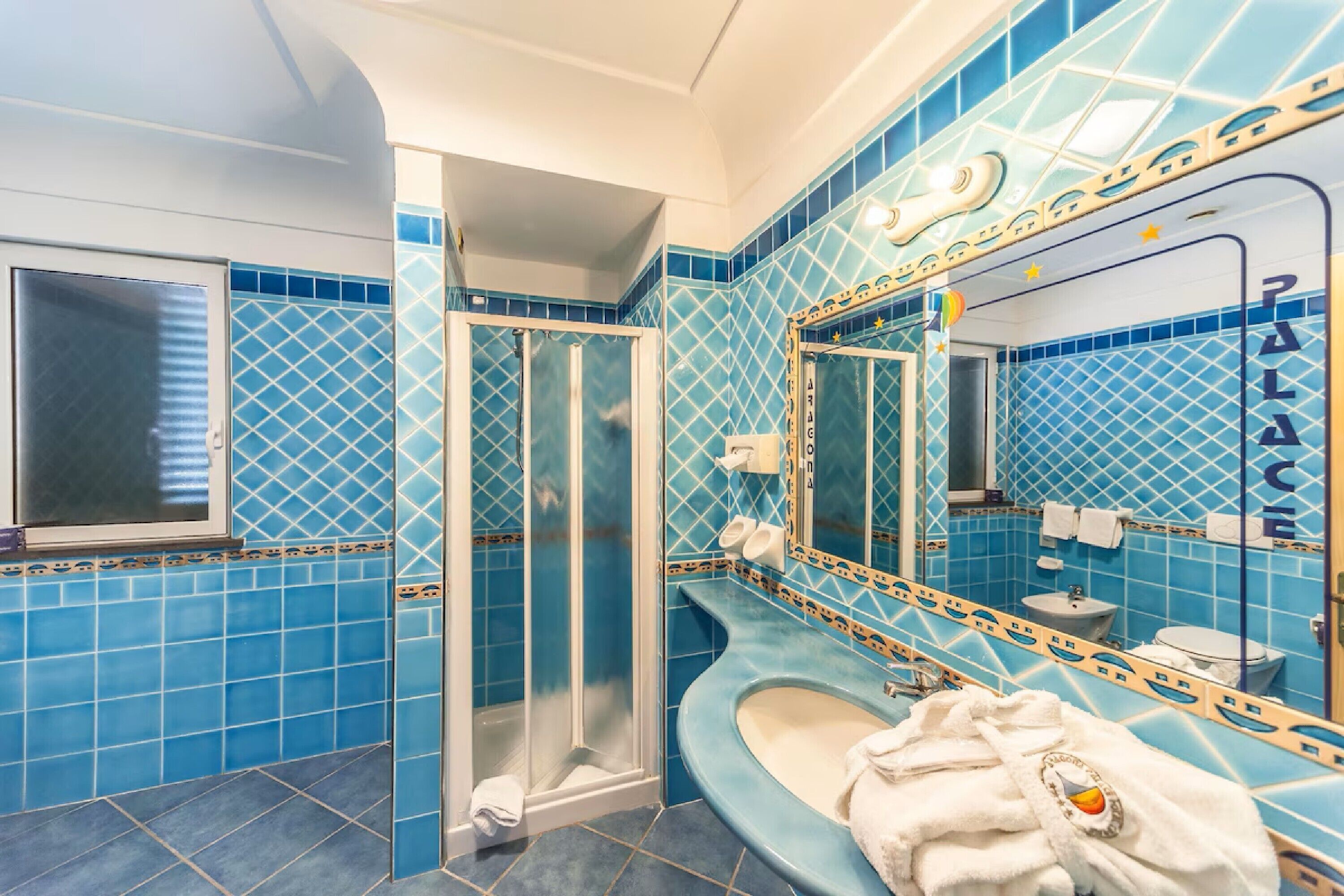 A bathroom with blue tiles, a glass shower enclosure, a sink, and a mirror with a decorative frame.