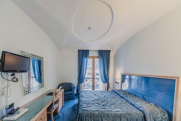 A bedroom with a bed, a desk, a chair, a television, and a window with curtains.