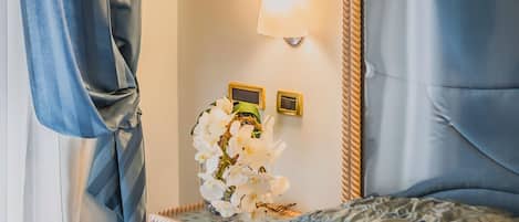 Una cama bien tendida con un cabecero azul, una mesita de noche con una lámpara y un jarrón con flores blancas.