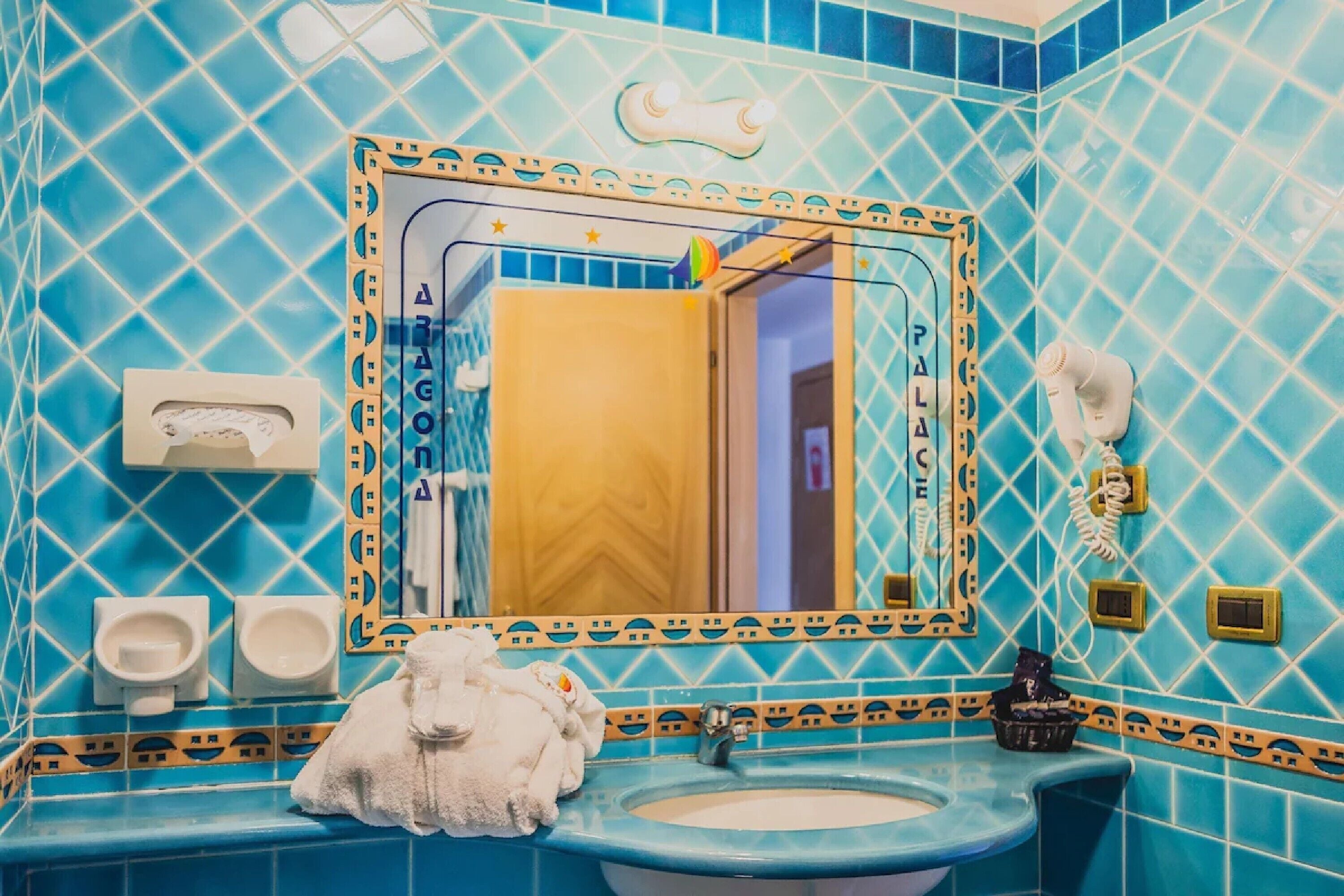 Casa de banho com azulejos estampados em azul, uma pia, um espelho, uma toalha e uma sanita.