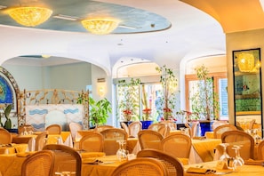 Een restaurant met ronde tafels, rieten stoelen en potplanten.