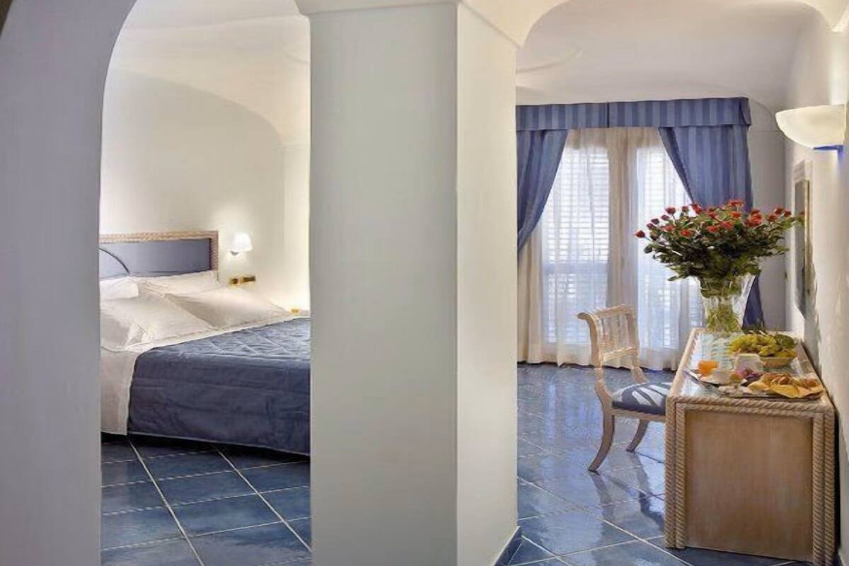 Ein Hotelzimmer mit Bett, Stuhl, Tisch mit Vase und einem Fenster mit Vorhängen.