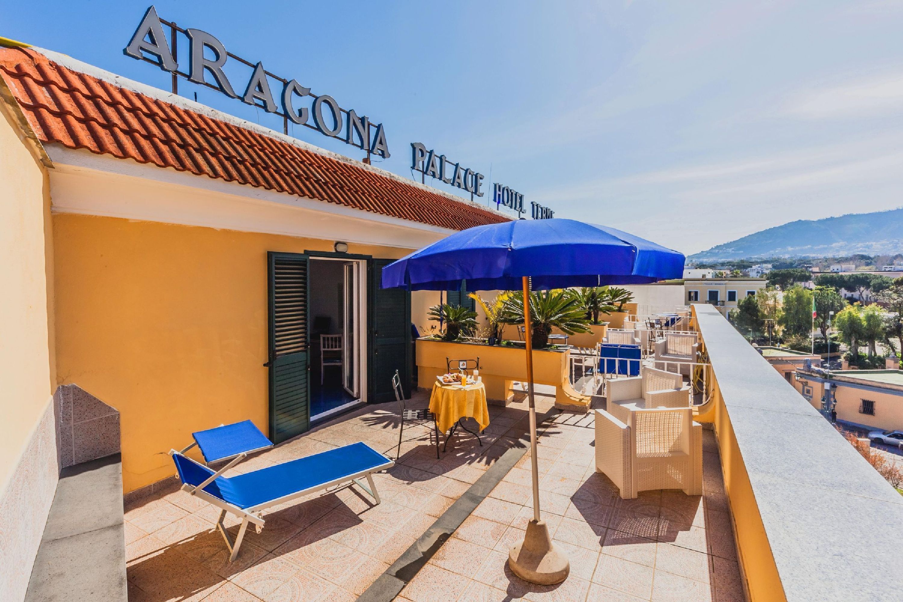 A rooftop terrace with a sign reading 'ARACONA PALACE HOTEL,' outdoor furniture, and a view of the landscape.
