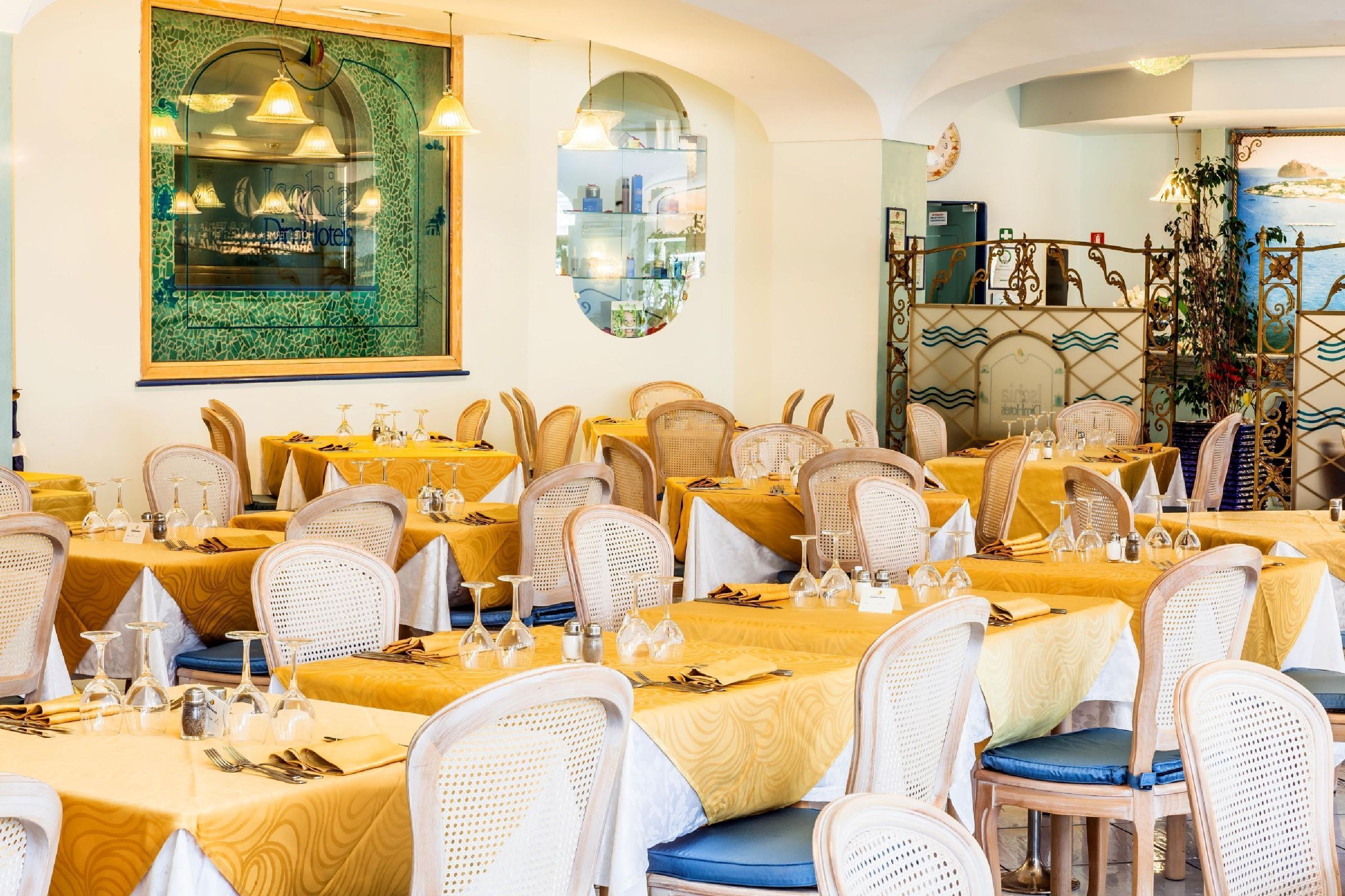 A restaurant with round tables, wicker chairs, and yellow tablecloths.