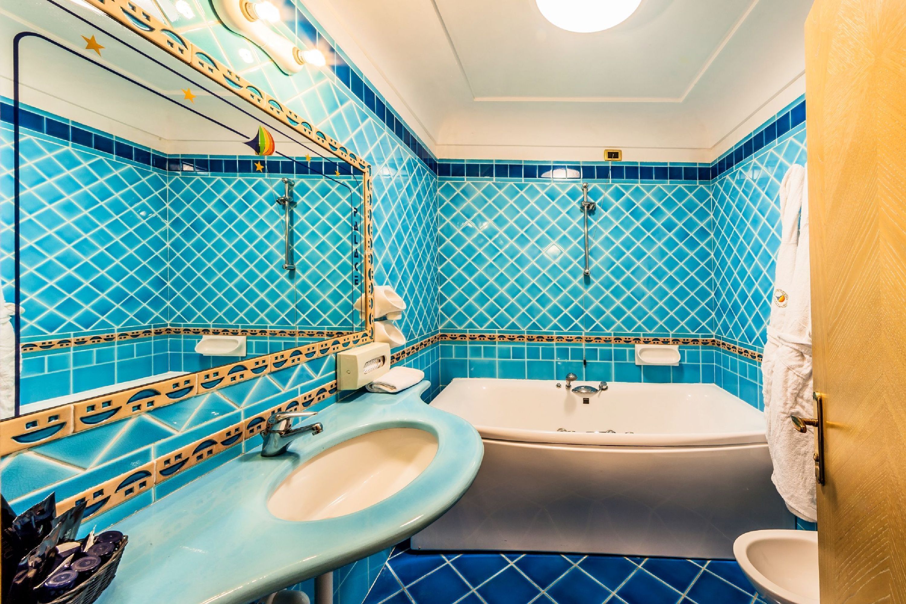 A bathroom with blue tiled walls, a sink, a bathtub, and a mirror.