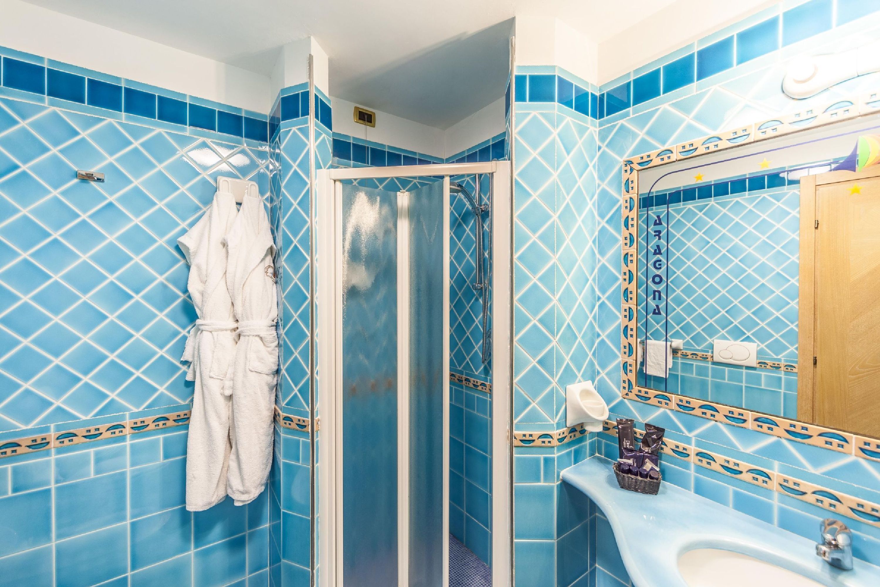 A bathroom with blue patterned tiles, a glass-enclosed shower, a white bathtub, and a sink with toiletries.