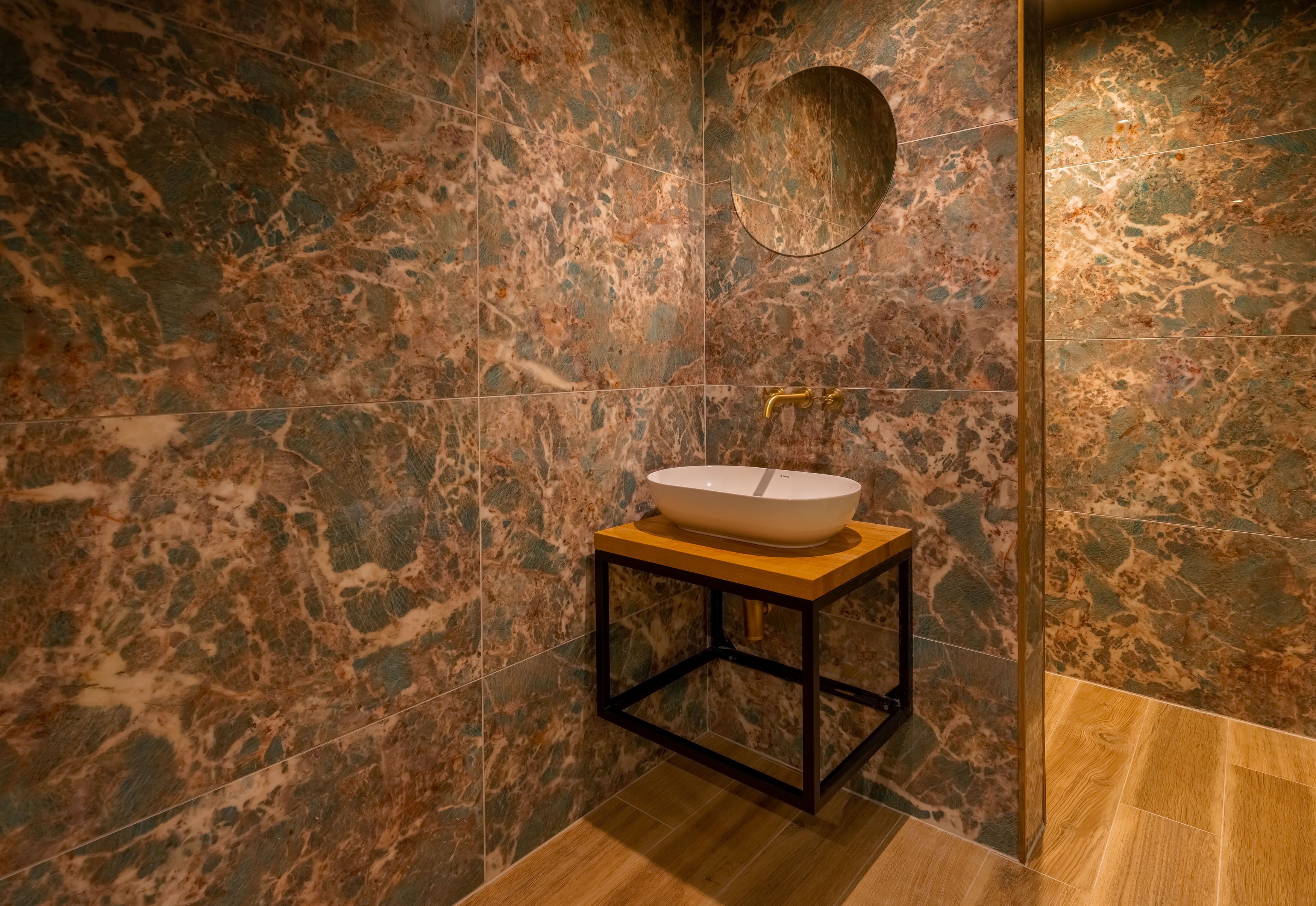 A bathroom with a marble wall, a wooden vanity, and a sink.