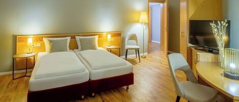 Habitación de hotel con dos camas, una televisión, un escritorio con silla y una lámpara.
