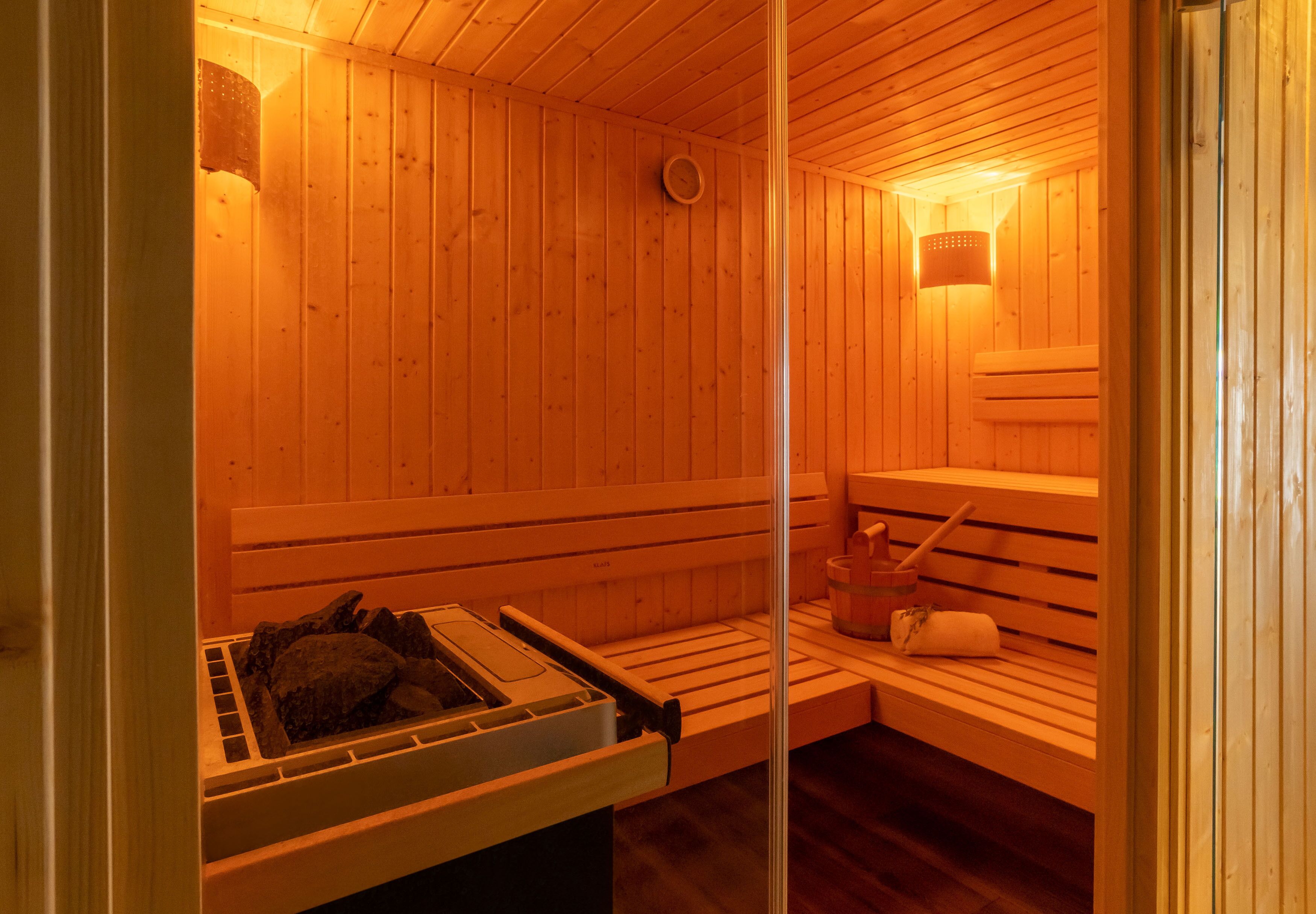 Una sauna con bancos de madera, un calentador para bancos y una cuenca de piedra.