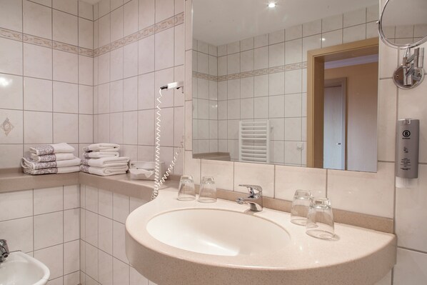 Un baño con lavamanos, espejo, toallero y ducha.