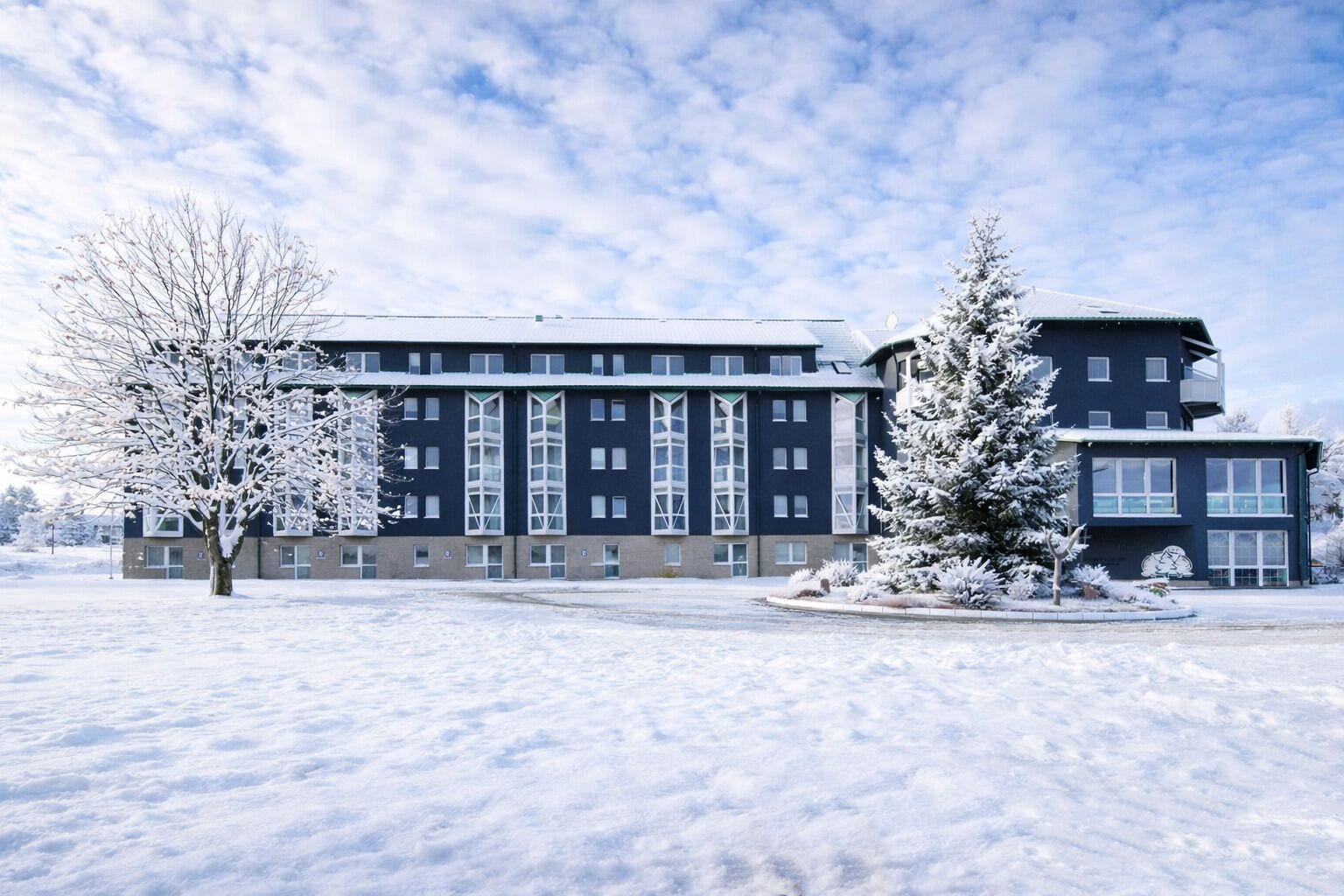 Un hôtel à plusieurs étages, doté d’une façade symétrique, de grandes fenêtres et surplombant un paysage enneigé.