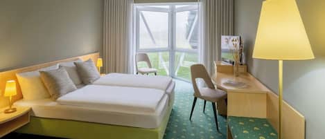 A hotel room with a bed, two bedside lamps, a desk with a lamp, a chair, and a large window.